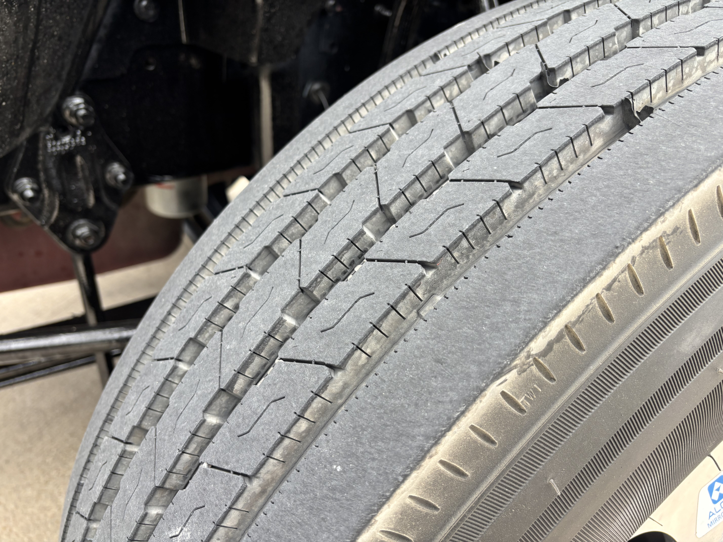 Front tire and wheel well of a Mack AN64T70 truck with tread visible on tire and part of the chassis in view.
