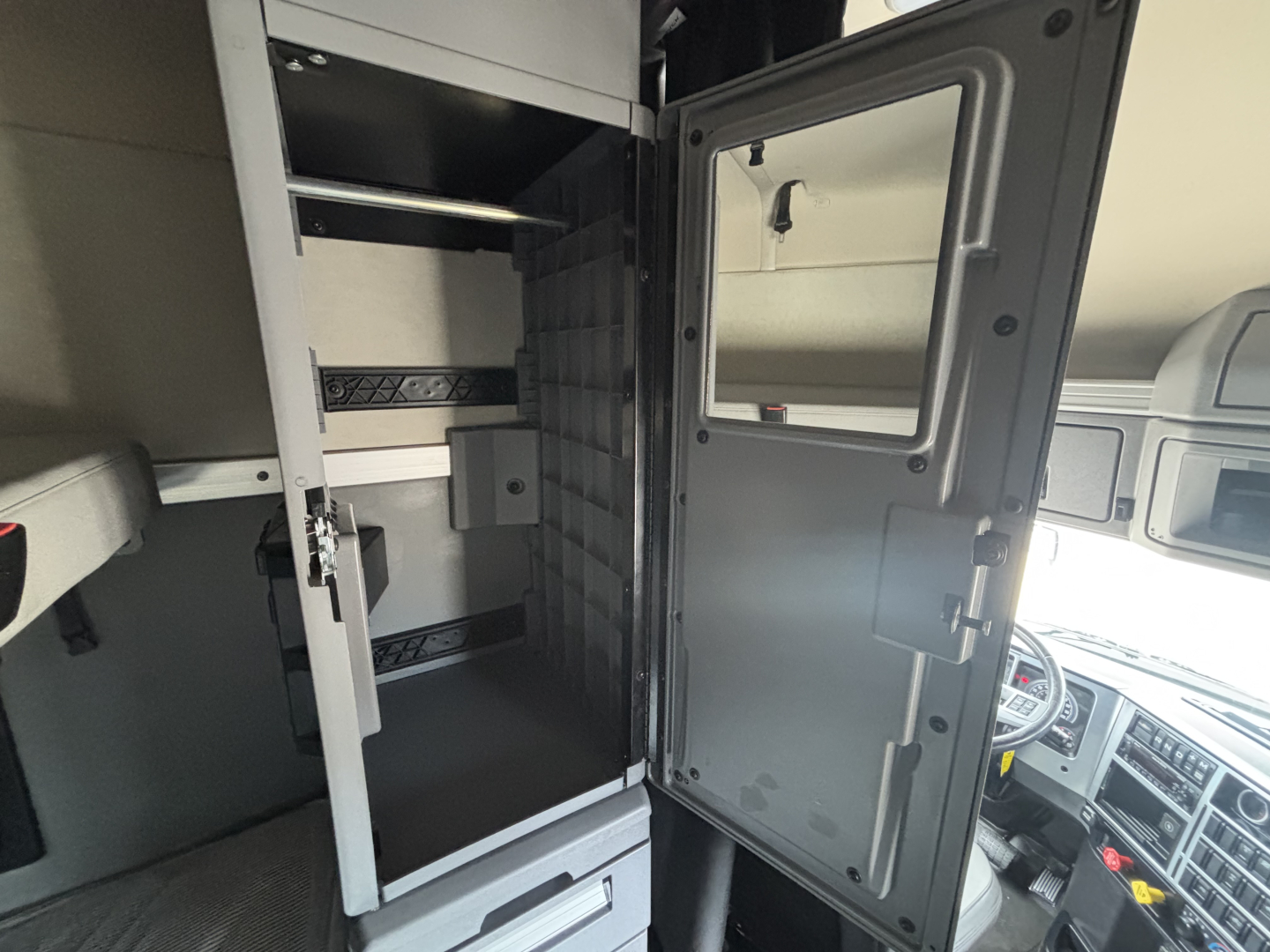 Truck interior showing cab area with tall metal cabinet and open refrigerator/freezer unit inside sleeper berth.