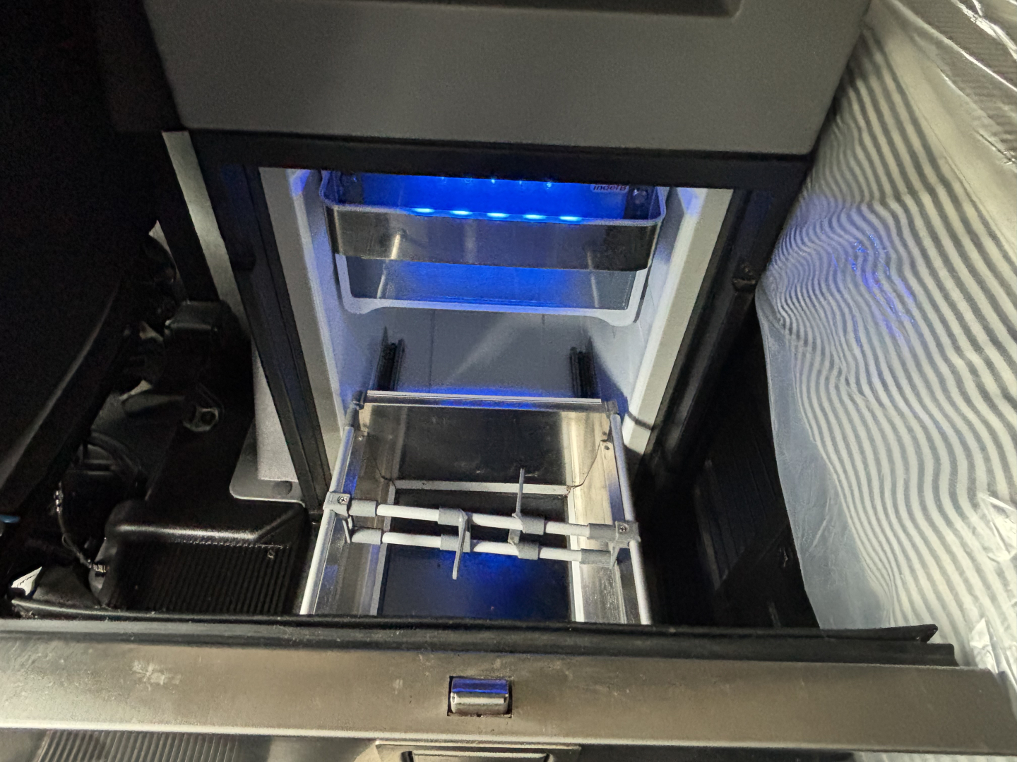 Truck interior showing a center console area with a blue-lit glovebox/locker and a metal slide-out tray.