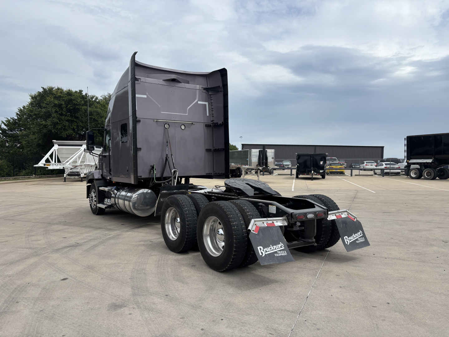 A Mack AN64T70 sleeper tractor rear view showing dual rear axles and Mack mud flaps with stock tires and parking lot background.