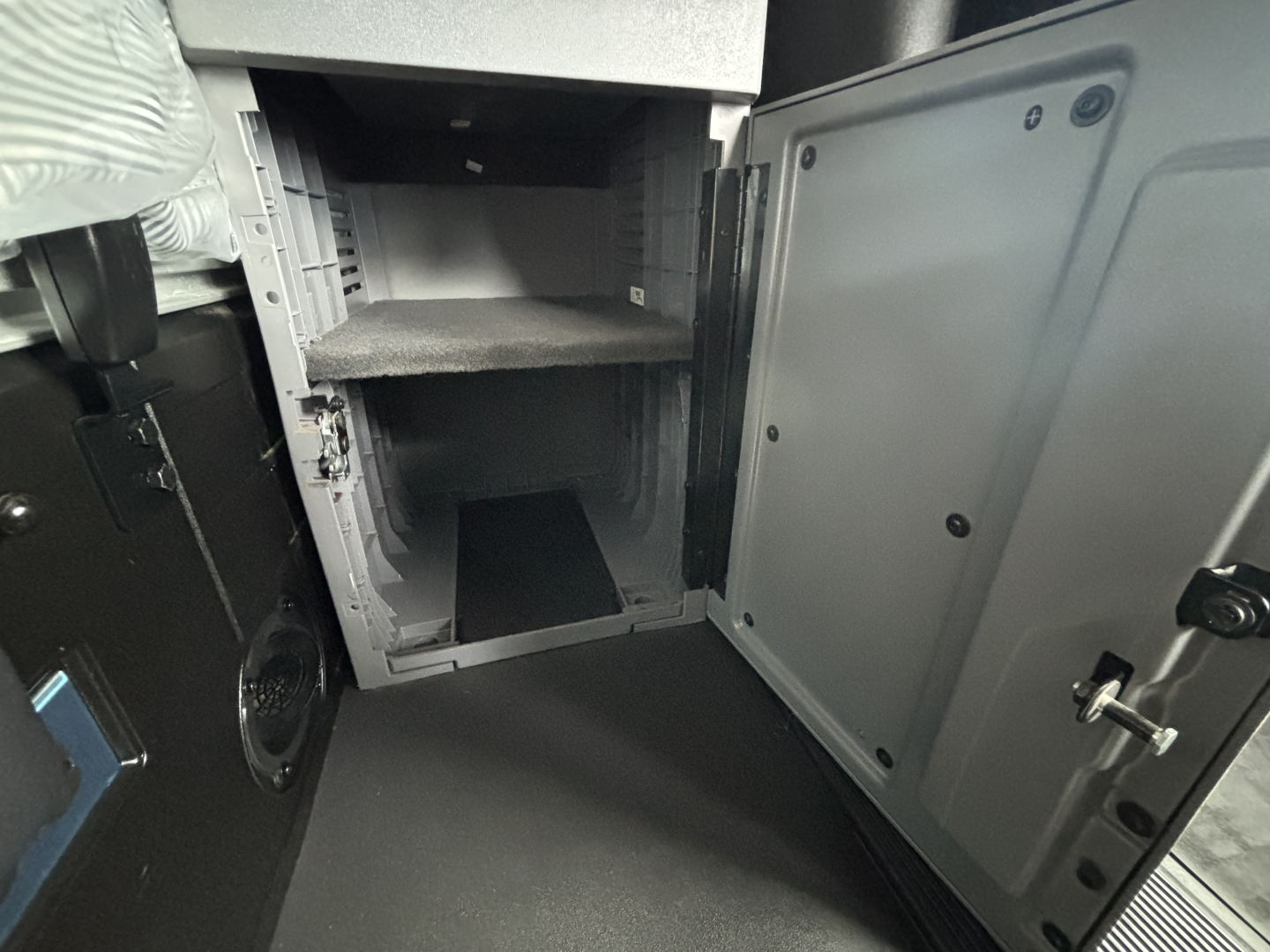 Truck cab area showing interior storage compartments and open lower locker with shelves in a Mack AN64T70 sleeper tractor.