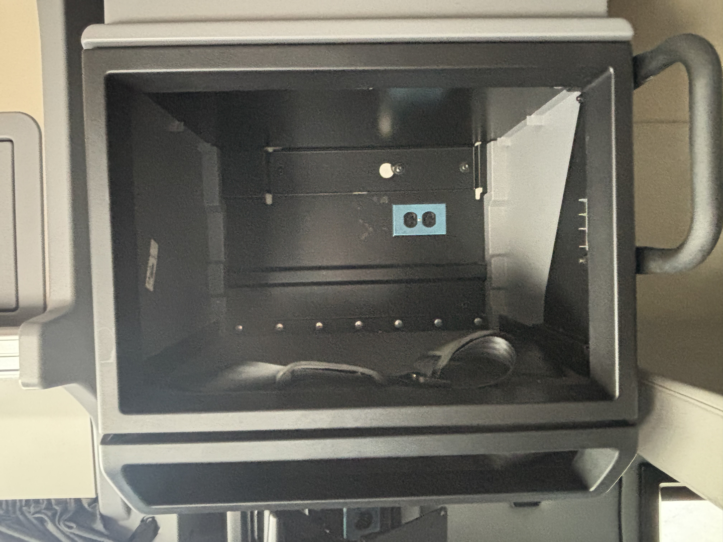 Truck cab interior storage compartment with blue electrical outlet panel and wiring visible.
