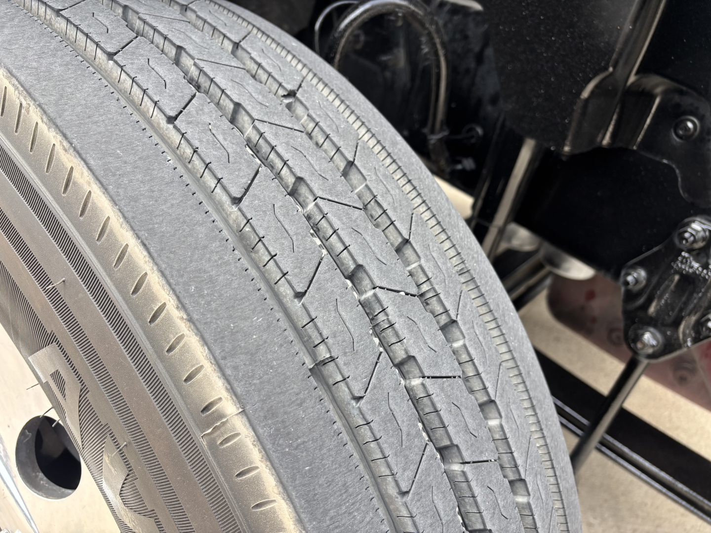 Tire tread close-up on Mack AN64T70 truck; visible text on tire sidewall includes punctured tread pattern and part of wheel hub and suspension components.