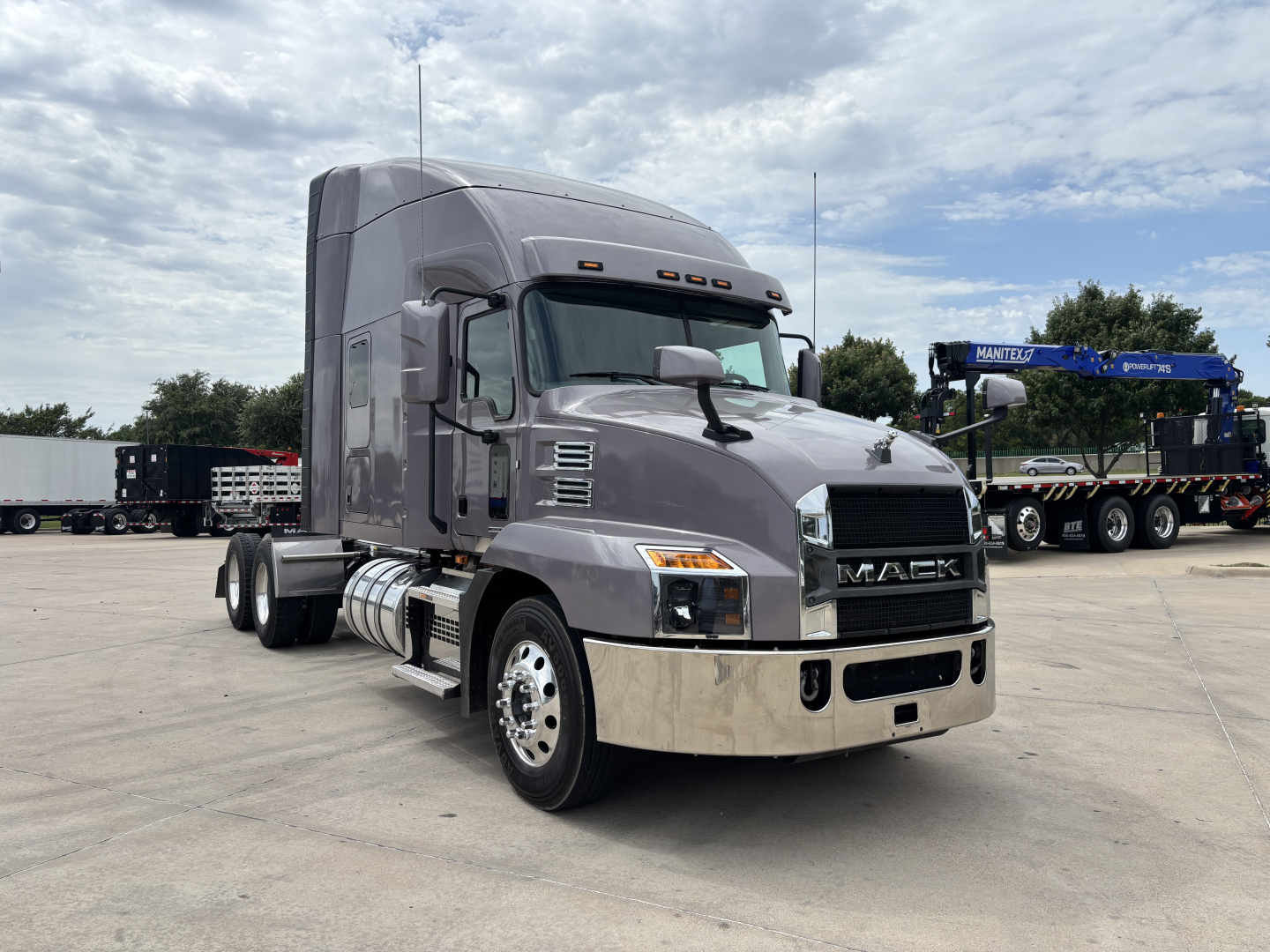 Mack AN64T70 conventional sleeper truck in a parking lot, gray cab with chrome front bumper, Mack logo on grille, side fuel tanks, dual rear axles.