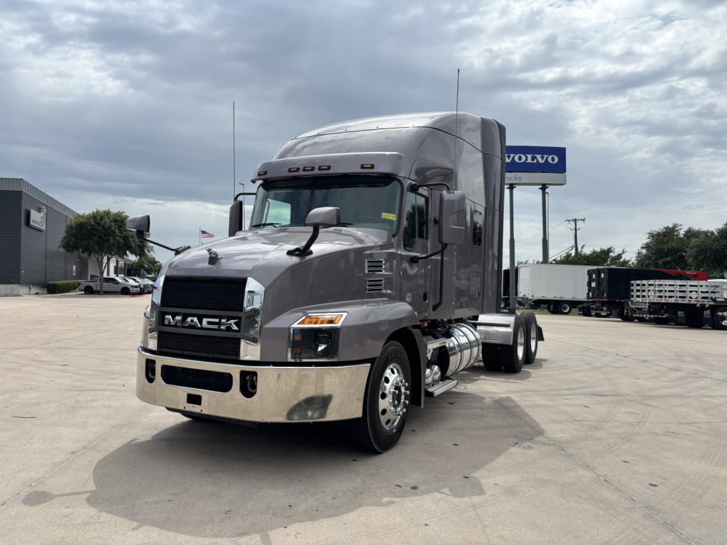 Mack AN64T70 conventional sleeper truck in a parking lot, front-left view with chrome bumper, grille, and fuel tanks visible.