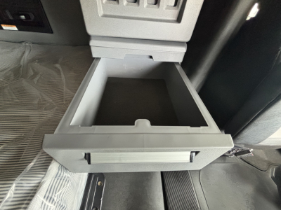 Open center console drawer in a Mack AN64T70 cab showing a shallow storage drawer with light gray plastic and surrounding dashboard area.