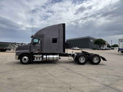 Tractor unit side view of a used 2023 Mack AN64T70 conventional sleeper truck with gray exterior, visible fuel tanks, and tandem rear axles.