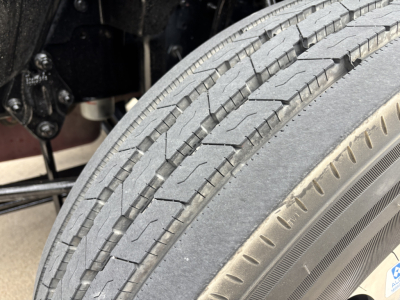 Front tire and wheel well of a Mack AN64T70 truck with tread visible on tire and part of the chassis in view.