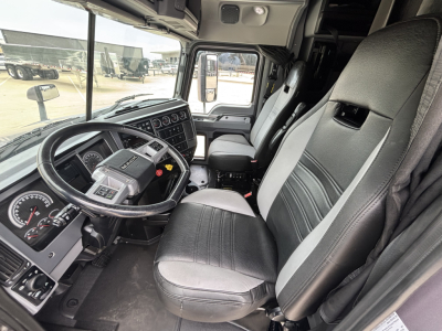 Truck cab interior showing steering wheel, dashboard, and two front seats in a Mack AN64T70 sleeper cab.