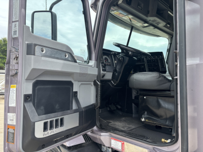 Truck cab interior view of a 2023 Mack AN64T70 with driver seat and dashboard visible, open door showing interior panels and steps.
