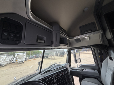 Mack AN64T70 truck cab interior overhead panel and dashboard visible from driver seat. Cabin storage shelves, overhead console, and window view with exterior yard.