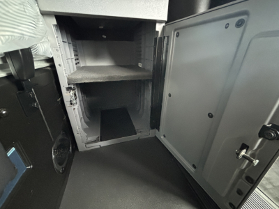 Truck cab area showing interior storage compartments and open lower locker with shelves in a Mack AN64T70 sleeper tractor.