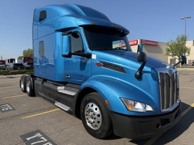 Peterbilt 579 tractor in blue parked front-left view with sleeper cab, chrome grille, dual rear axles, and black bumper; no visible warning labels legible.