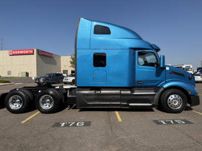 Peterbilt 579 truck side profile showing blue sleeper cab and chassis with triple rear axles in a parking lot.