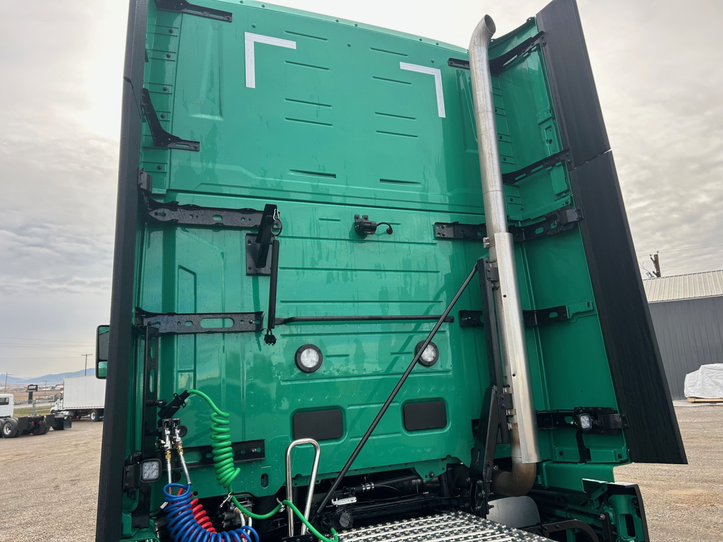Green Volvo VNL cab rear view with exhaust stack and rear frame, truck body panels and hinges visible.