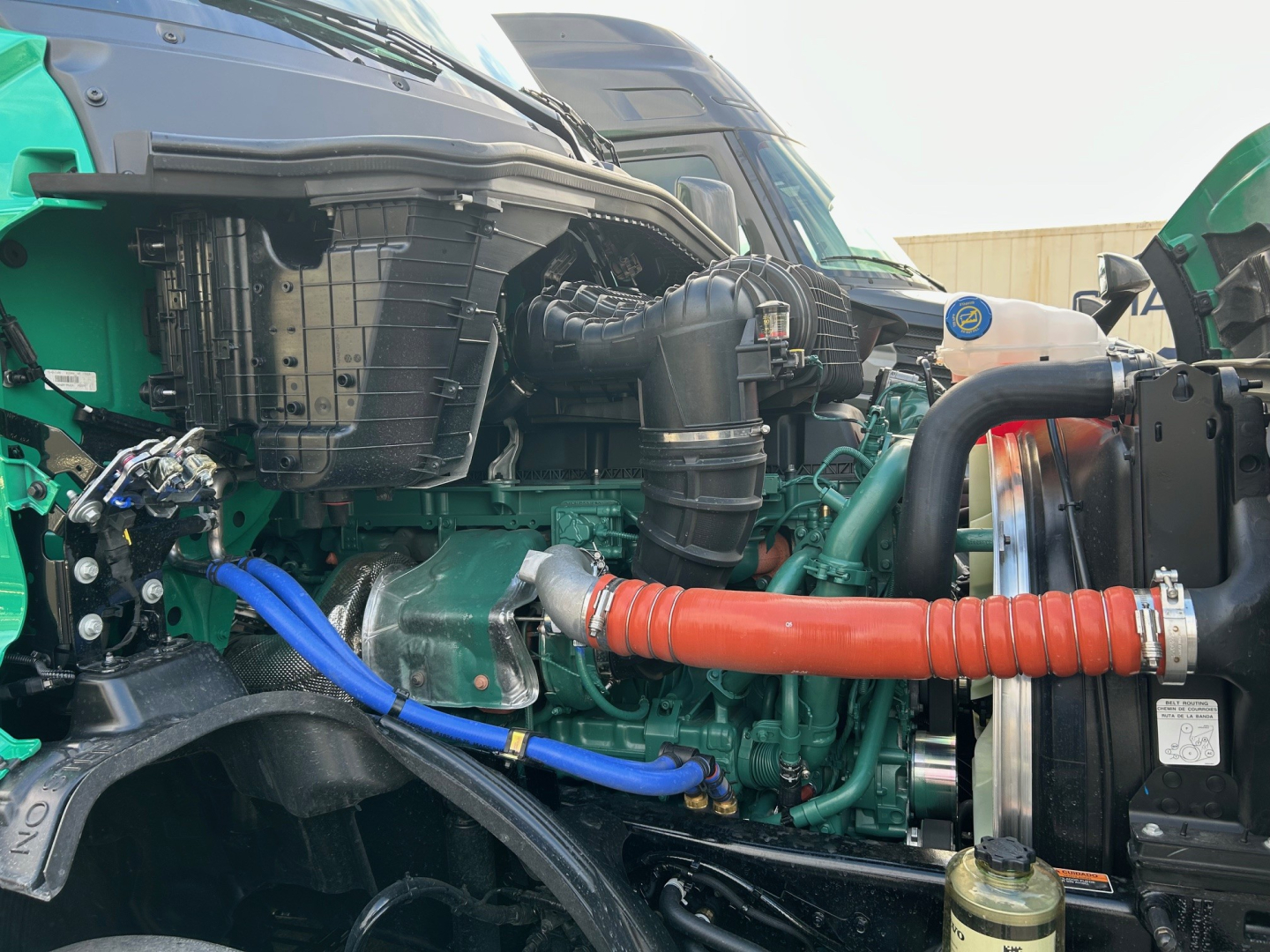 Engine bay of a new Volvo VNL64T860 truck showing radiator, hoses, and engine components with blue and red/orange coolant/air hoses.