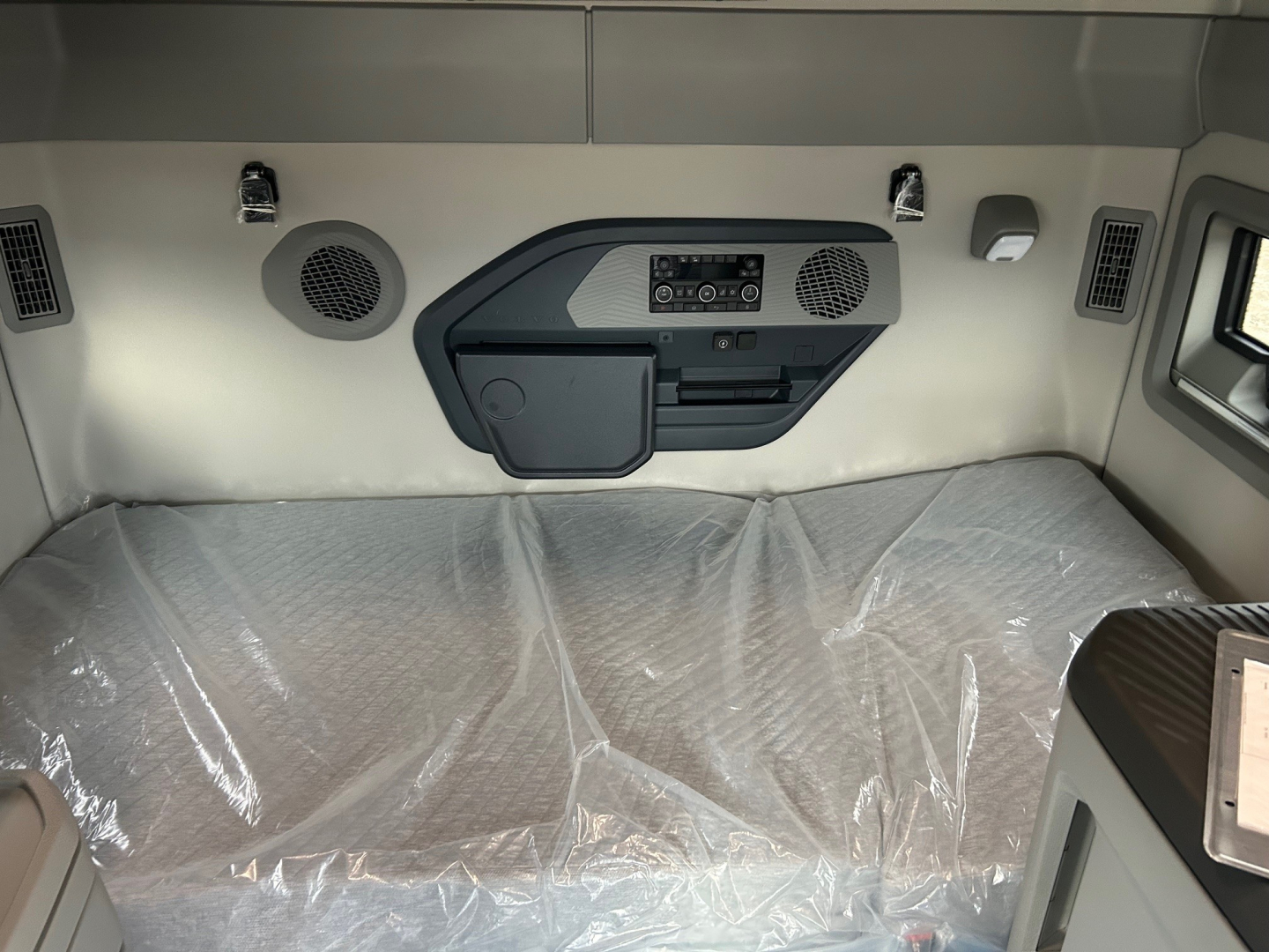Volvo VNL64T860 sleeper cab interior showing overhead control panel, speakers, storage pockets, and covered bedding area.