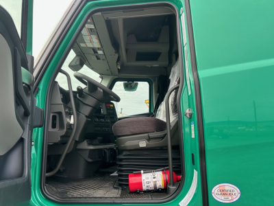 Volvo VNL truck interior cockpit view with green exterior, driver seat, steering wheel, and a red fire extinguisher on the floor.