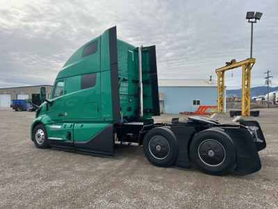 Volvo VNL truck tractor side view showing green cab with sleeper, rear wheels, and fifth wheel.