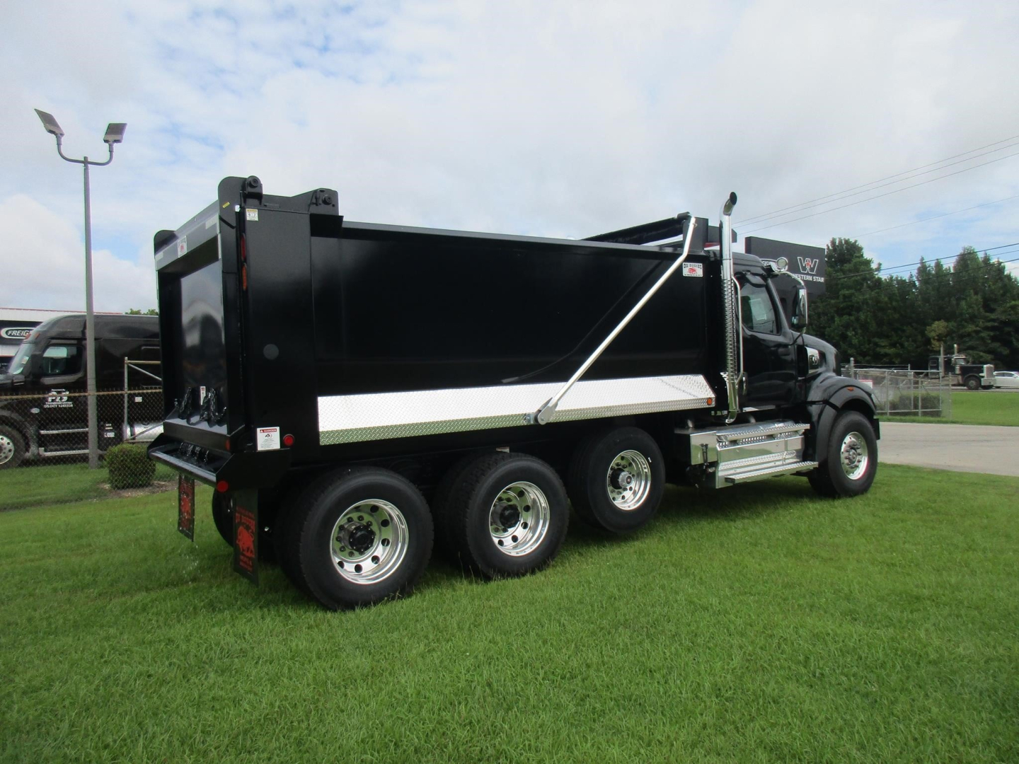 Dump truck with black dump body and chrome wheels, Western Star 49X, side view showing reinforcement bars and hydraulic mechanism.
