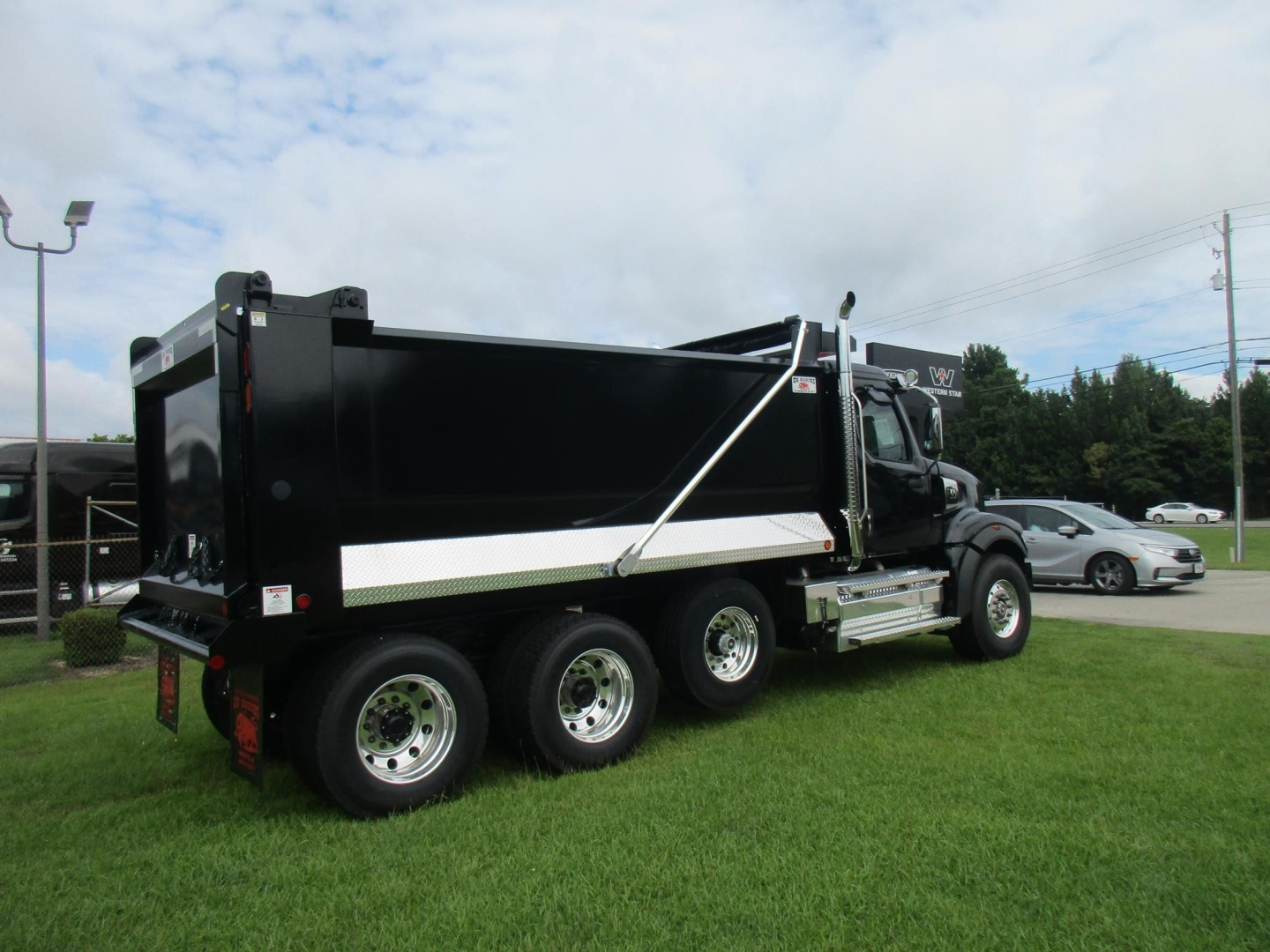 Dump truck showing side view of a black Western Star 49X dump truck with three rear axles and a white reflective strip along the cargo bed.