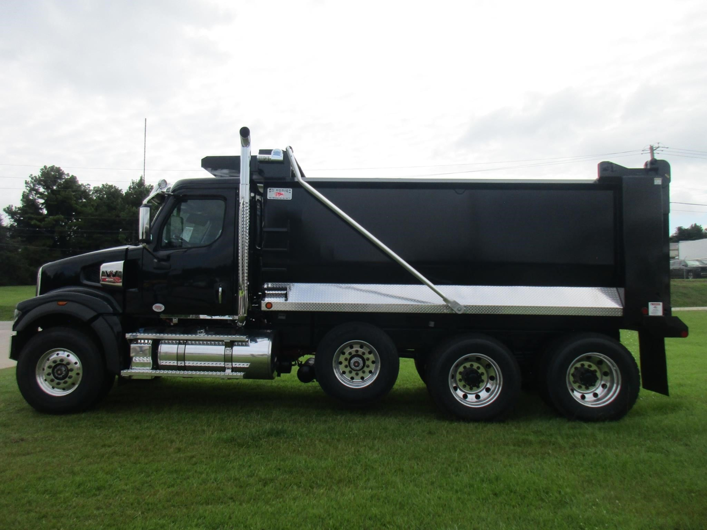 Dump truck side view showing Western Star 49X with black cab and large black dump body, chrome step rails, and silver stripe along side.
