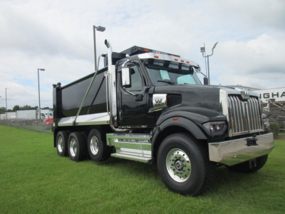 Dump truck, Western Star 49X, black cab with chrome grille, triple rear axles, large dump bed, daytime outdoor dealership lot.
