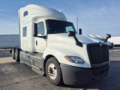 International LT625 truck in yard with sleeper cab and aerodynamic grille, side view showing front wheels and fuel tanks.