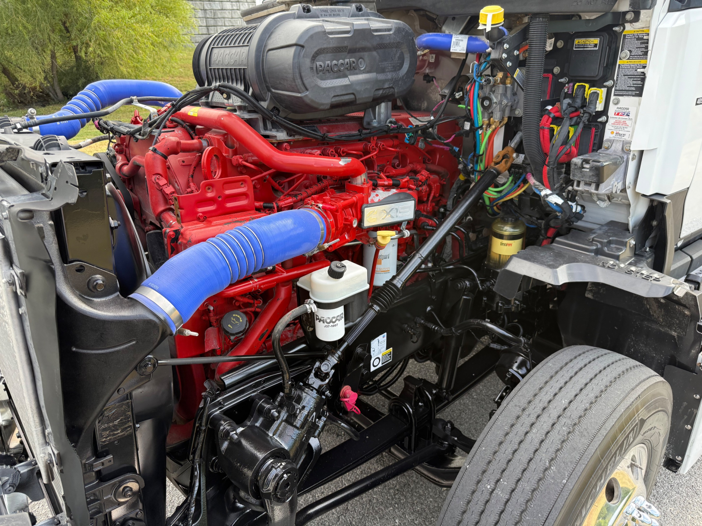 Kenworth T680 engine bay with red diesel engine, blue coolant hose, various connectors, and mechanical components visible.