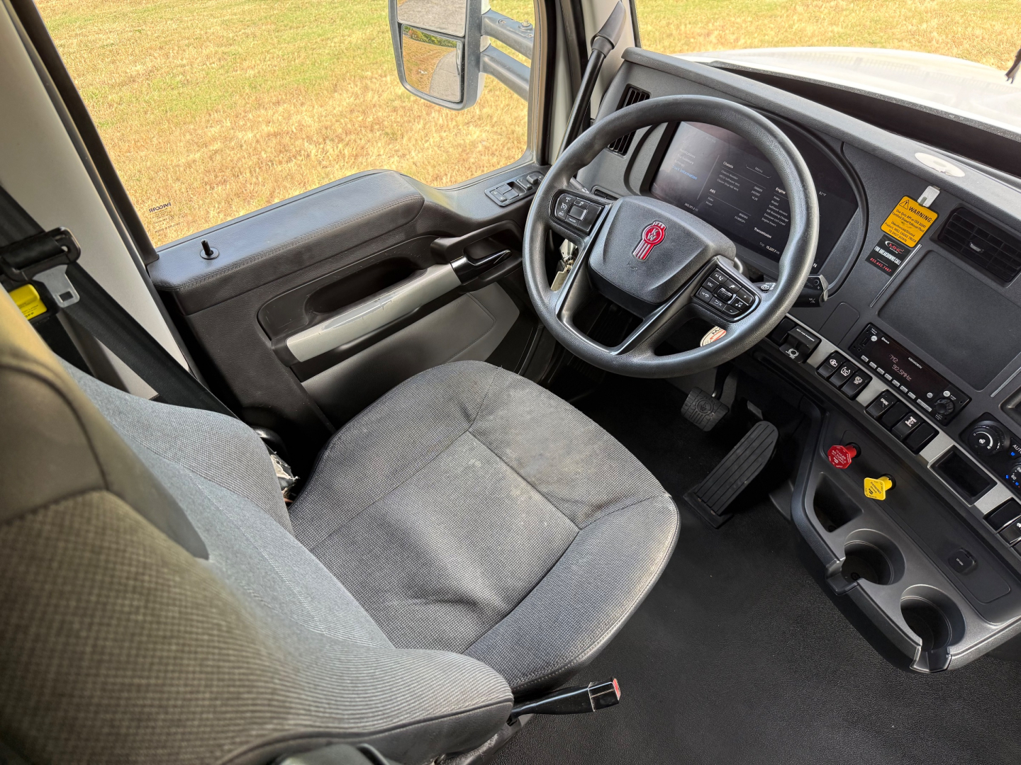 Kenworth T680 truck interior showing steering wheel with emblem, dashboard, driver seat, and center console.