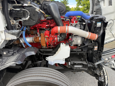 Kenworth T680 engine bay showing red engine block and blue hoses, intercooler piping, radiator support, and front wheel well.