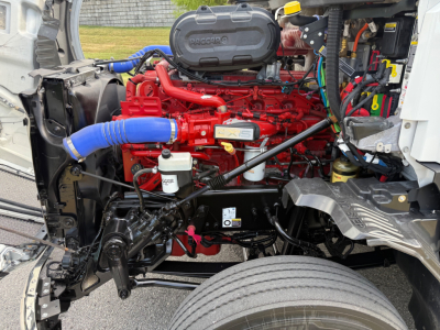 Kenworth T680 engine bay view showing red engine with blue intercooler hose, various black hoses, metal framework, and wiring harnesses.