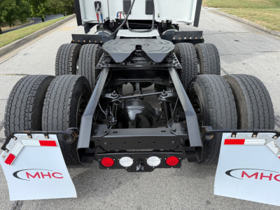 Rear view of a Kenworth T680 tractor chassis showing suspensions, dual rear axles, fifth wheel, and mudflaps with MHC branding.