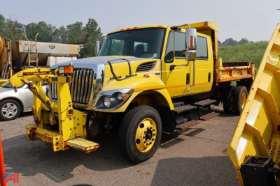 International WorkStar 7300 crew cab dump truck in yellow, front view with attached snow plow/loader equipment on front bumper and dump bed in background.