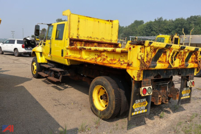Dump truck with yellow cab and bed showing rusted rear with black and yellow striped warning and mud flaps; International WorkStar 7300 crew cab dump truck.
