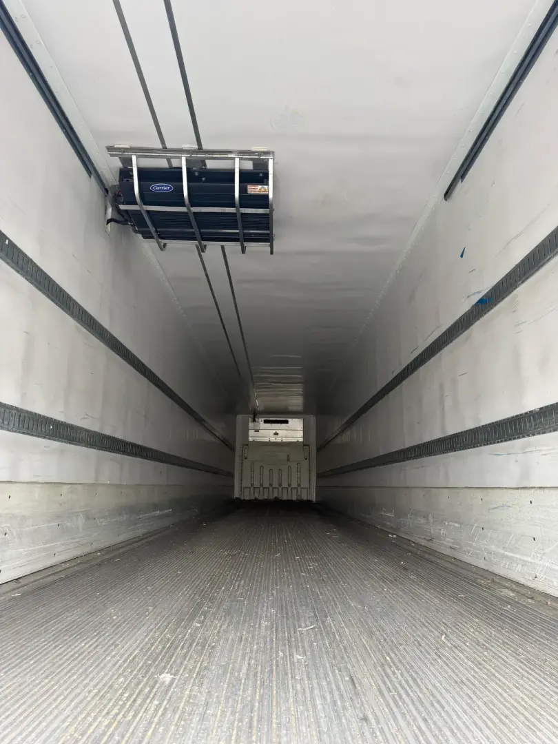 Interior of refrigerated trailer showing insulated walls, ceiling ceiling liner, side rails, and rear ramp door in cabin; no readable labels visible.