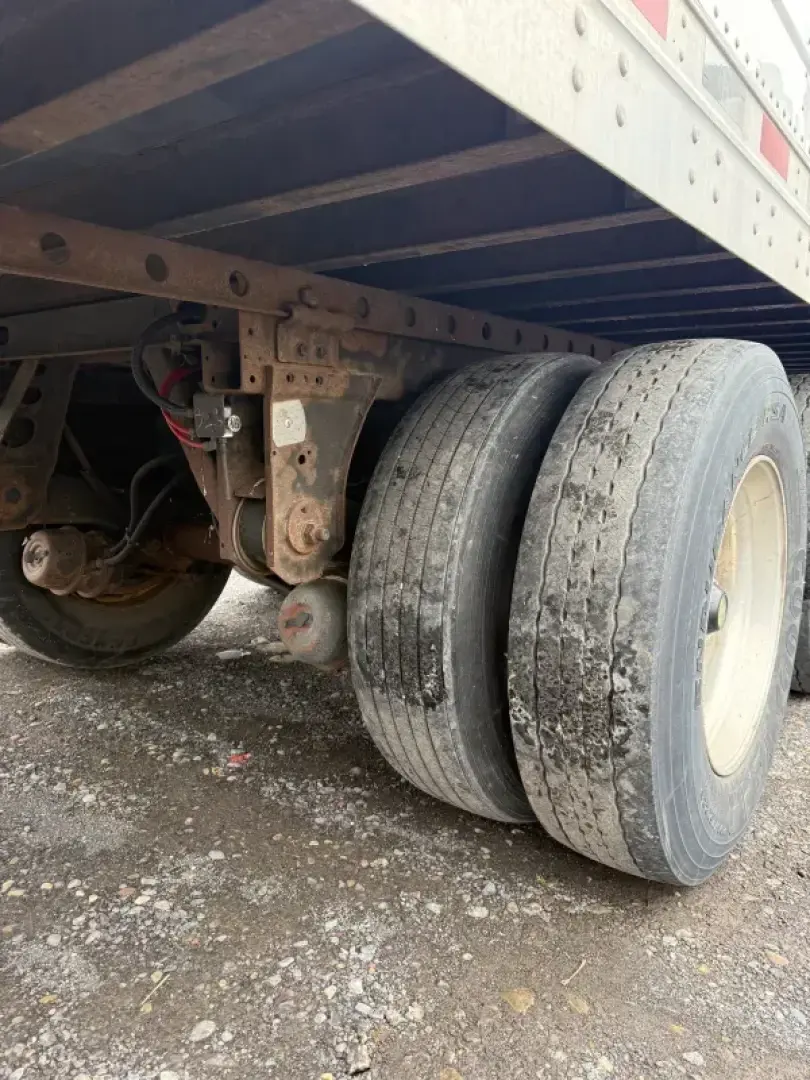 Dual rear trailer tires and undercarriage of a refrigerated trailer showing suspension components and frame members.