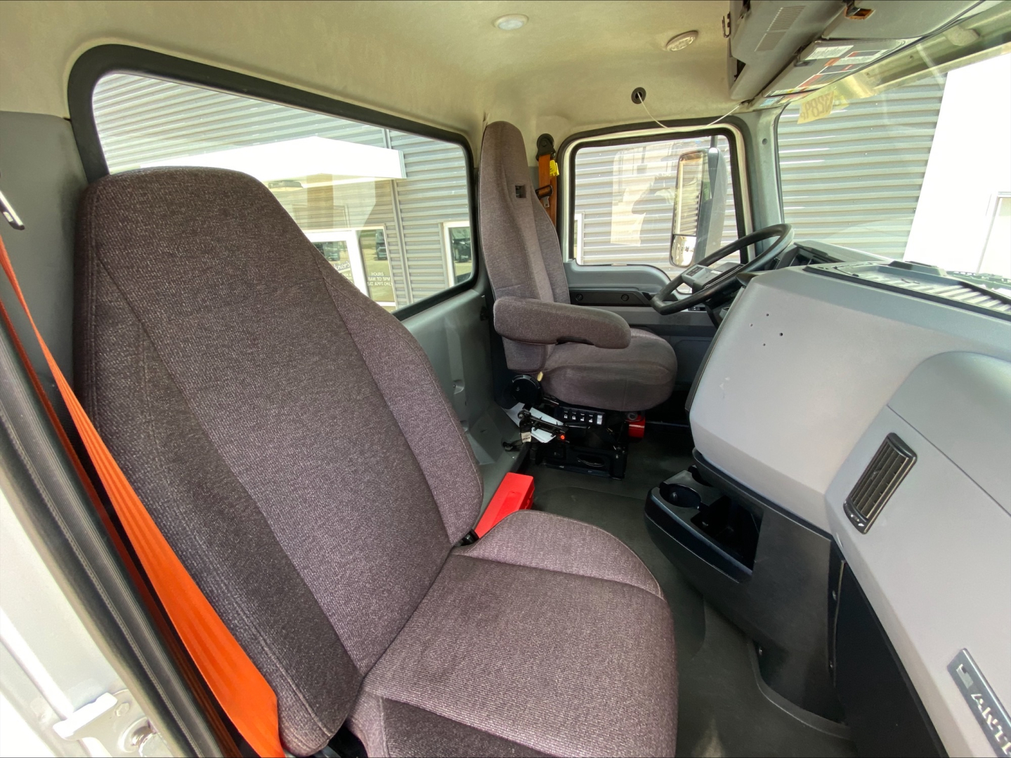 Truck cab interior of a 2021 Mack AN64T showing driver seat, steering wheel, dashboard, and passenger seat.