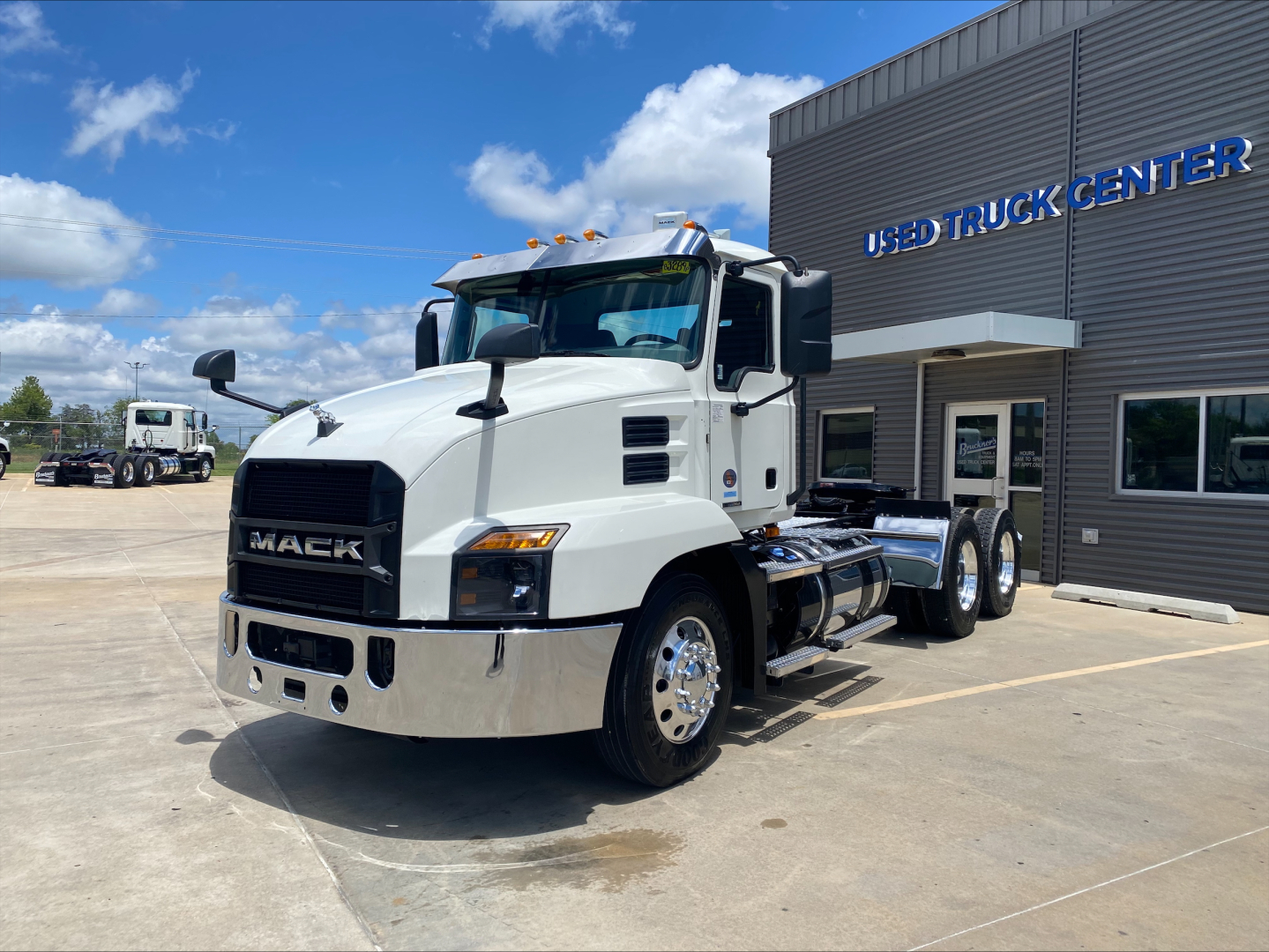 Mack AN64T conventional daycab truck parked in front of used truck center, white cab with chrome bumper, dual rear axles, and Mack grille.