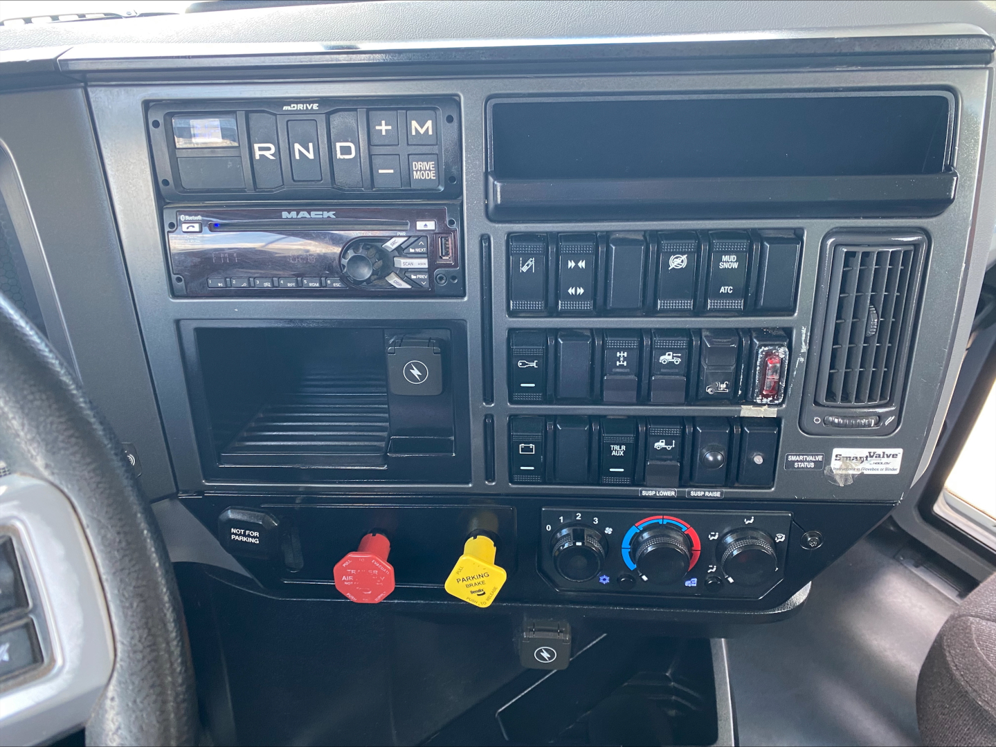 Dashboard of a 2021 Mack AN64T Daycab showing gear selector buttons (R N D + M), radio, climate controls, and red/blue knobs.