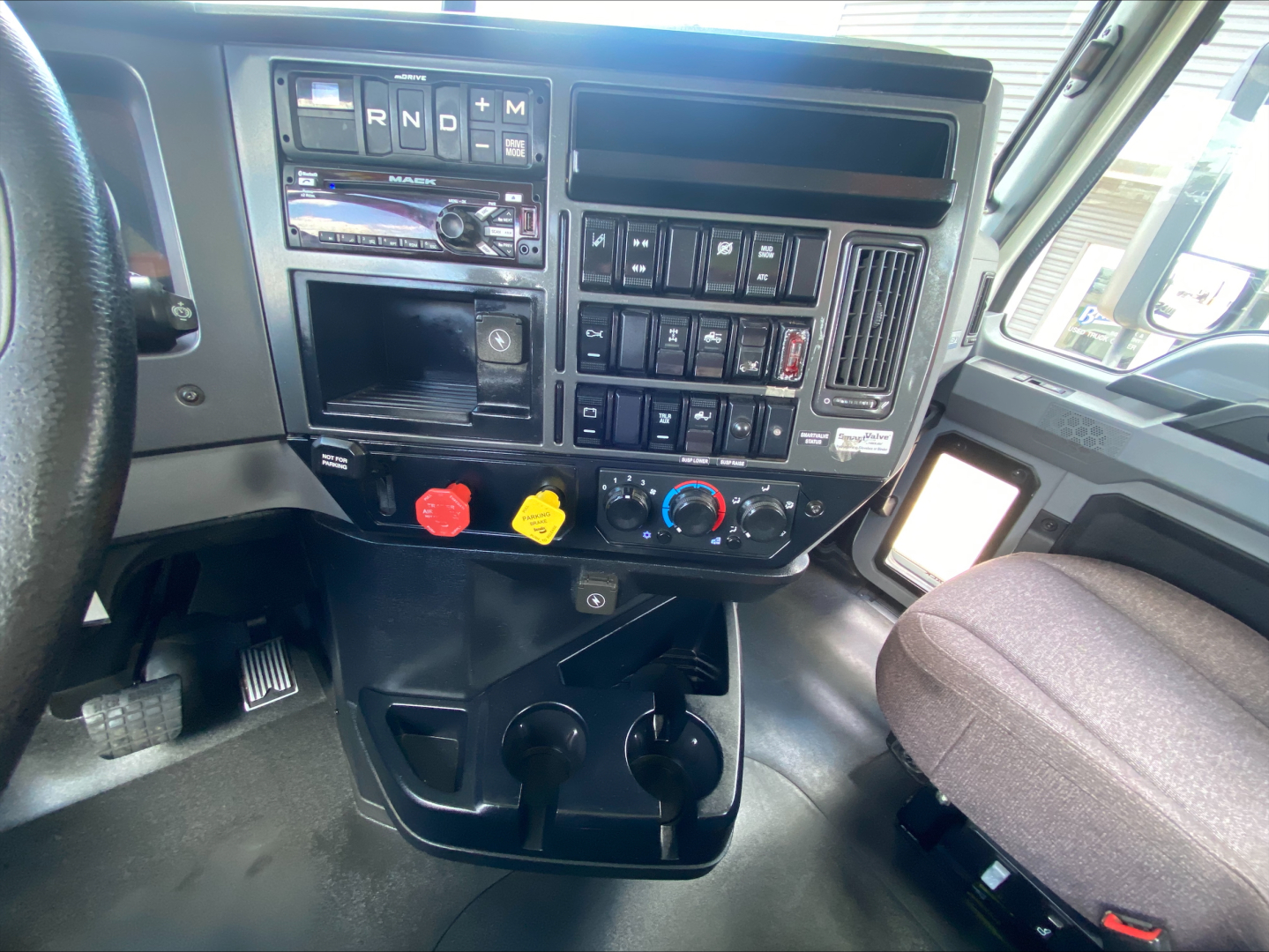 Dashboard area of a Mack AN64T truck cab showing steering wheel on left, control panel with R N D + M shifter, various switches, climate controls, and cup holders below.