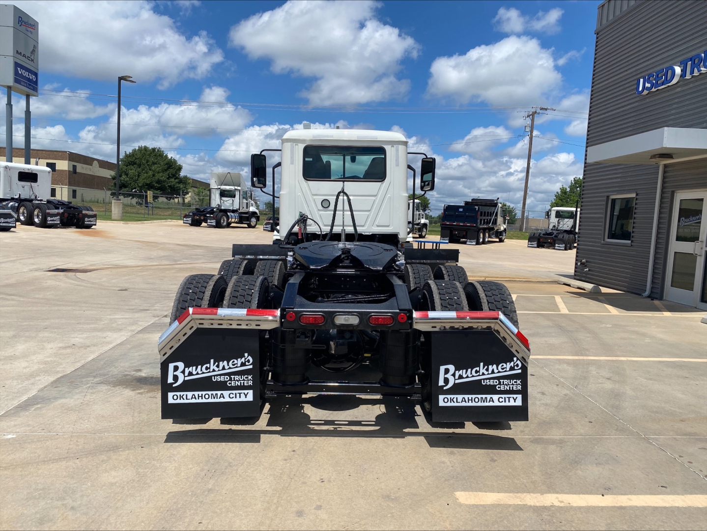 Truck chassis rear view with dual rear axles and mud flaps showing Bruckner’s Used Trucks Oklahoma City branding in a dealership lot.