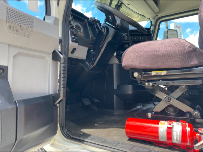 Truck cab interior of a 2021 Mack AN64T with driver seat, dashboard, steering wheel, and a red fire extinguisher on the floor; open door visible; VIN and stock info in listing.