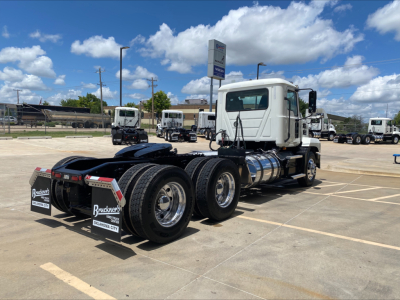 Truck chassis rear view showing dual rear axles and fifth-wheel area, white cab, in a dealership lot.
