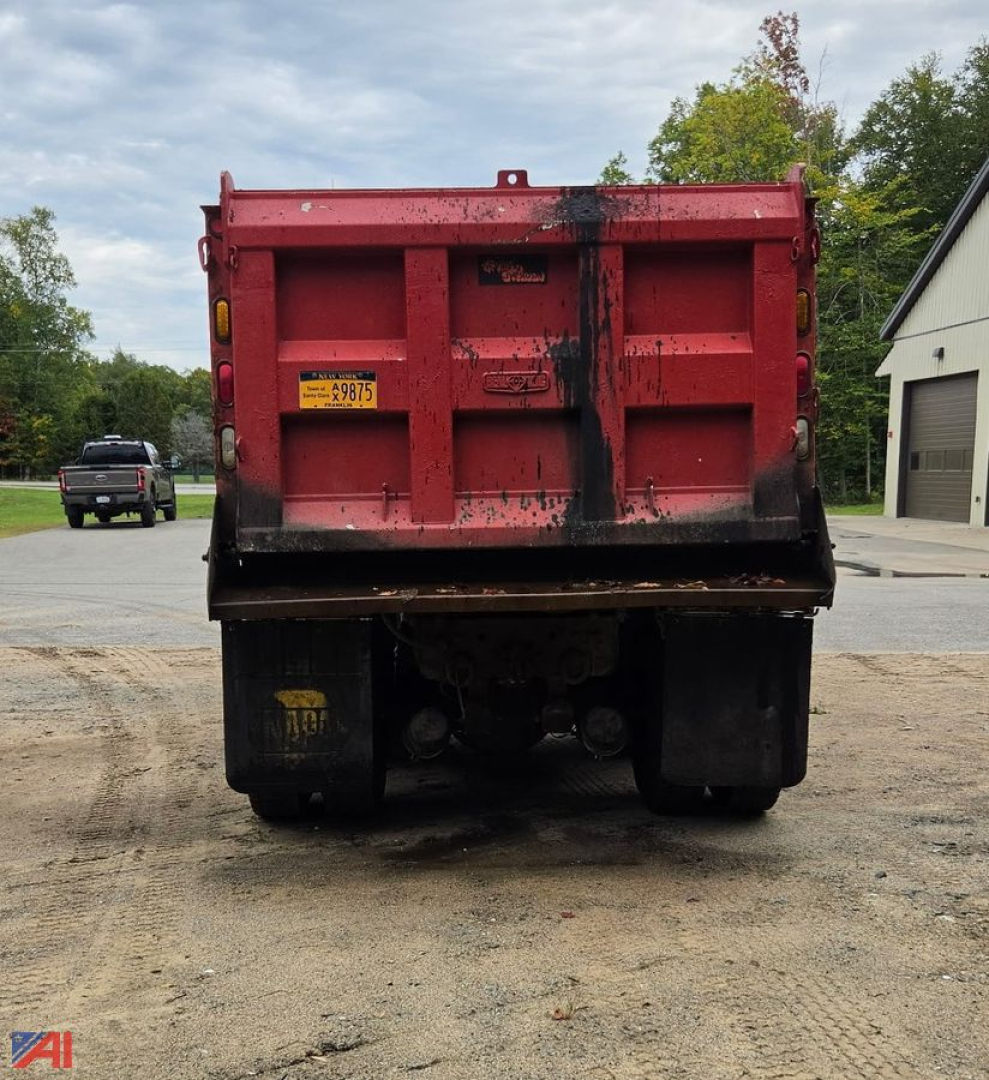 Dump truck rear showing red dump bed and black chassis with yellow license sticker and mud flaps.