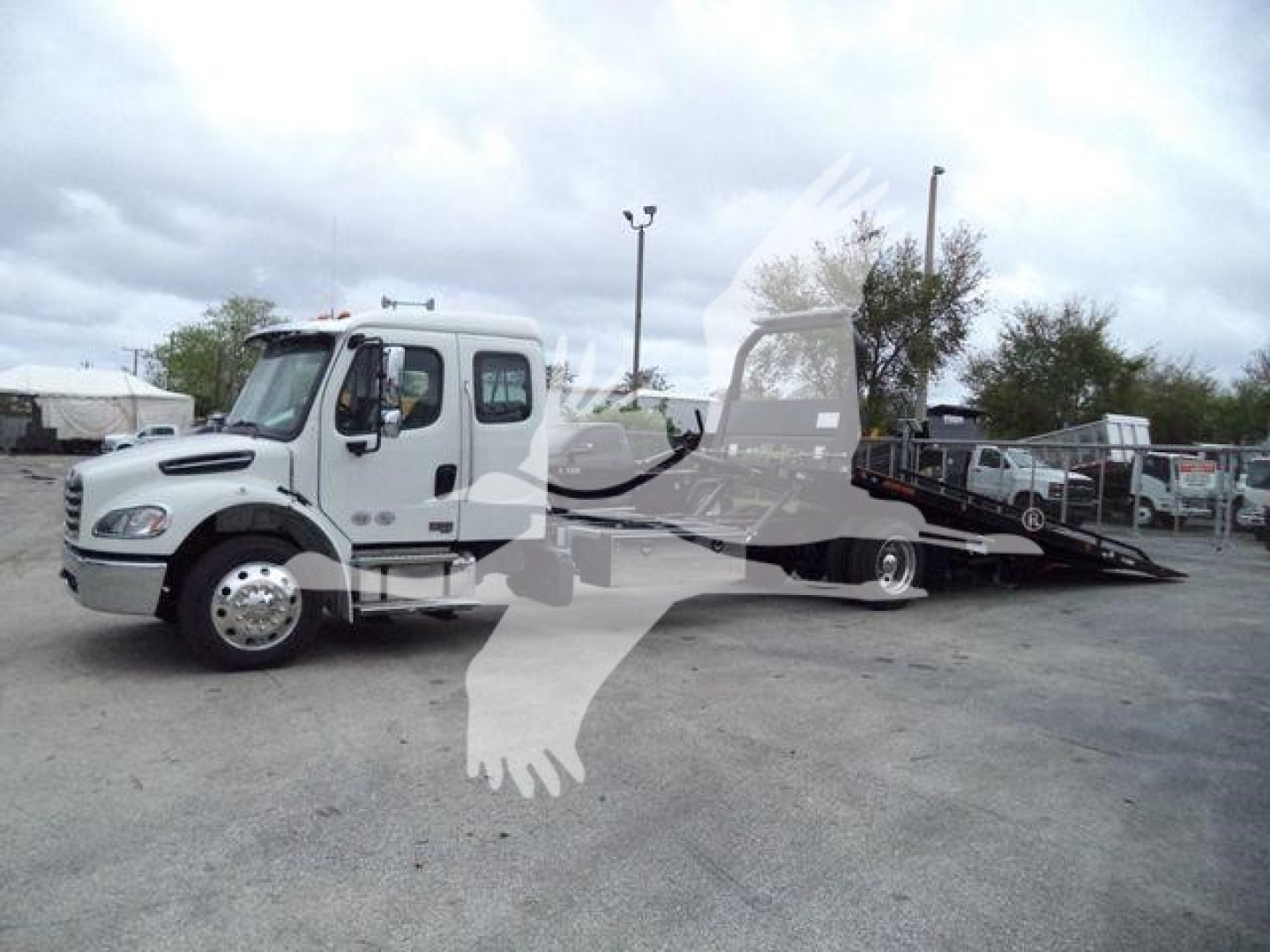Flatbed tow truck on lot, Freightliner M2 106 chassis visible with white cab and black tow bed.