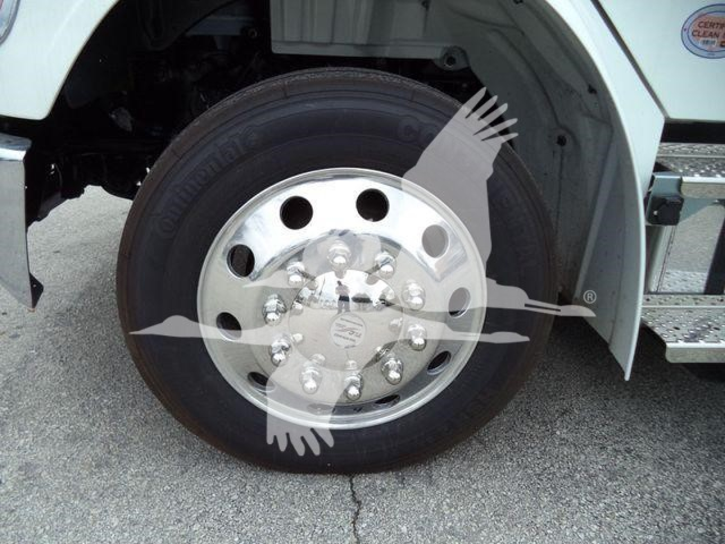 Front wheel and hub of a Freightliner M2 106 rollback truck with polished steel rim and tire, partial fender and steps visible.