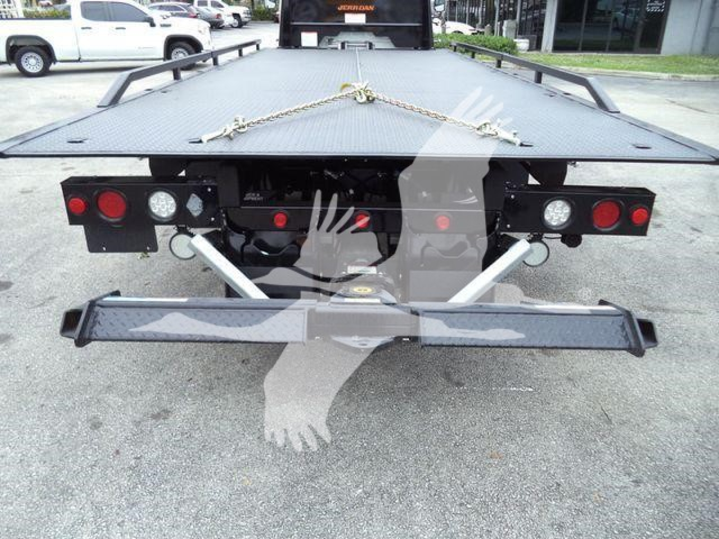 Flatbed rear view of a Freightliner M2 106 rollback truck showing taillights, bumper, and platform with chains.