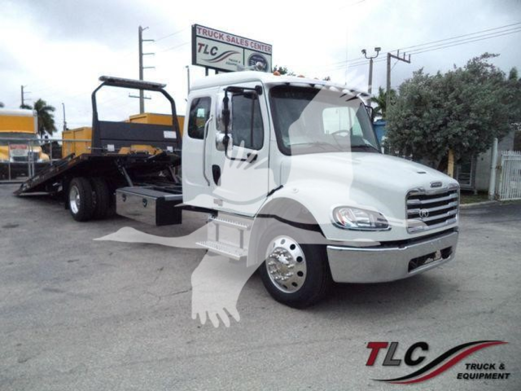 Front-left view of a white Freightliner M2 106 rollback truck with flatbed, chrome grille, and dual rear axle setup.