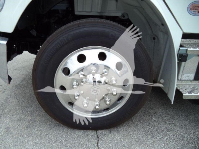 Front wheel and hub of a Freightliner M2 106 rollback truck with polished steel rim and tire, partial fender and steps visible.
